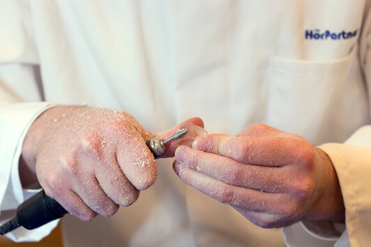 Ein Hörakustiker passt ein Hörgerät handwerklich präzise mit Spezialwerkzeug an.